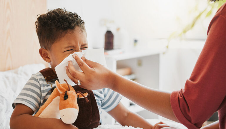 Young boy sick in bed with parent holding tissue to his nose