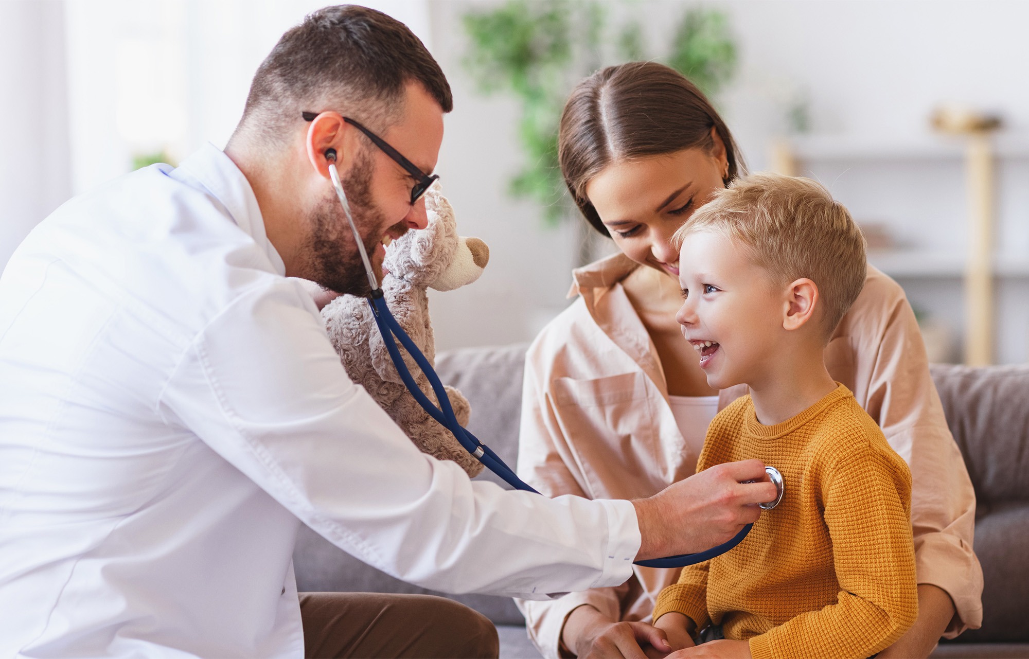 Male doctor using stethoscope with young boy and mother