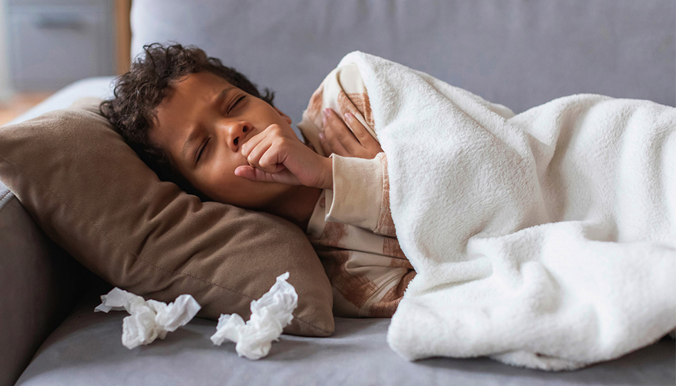Young sick boy on couch coughing with tissues